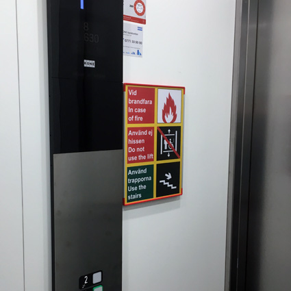Signcode A4 med signalröda kanter inuti hiss informerar om att hissen ej får användas vid brand.